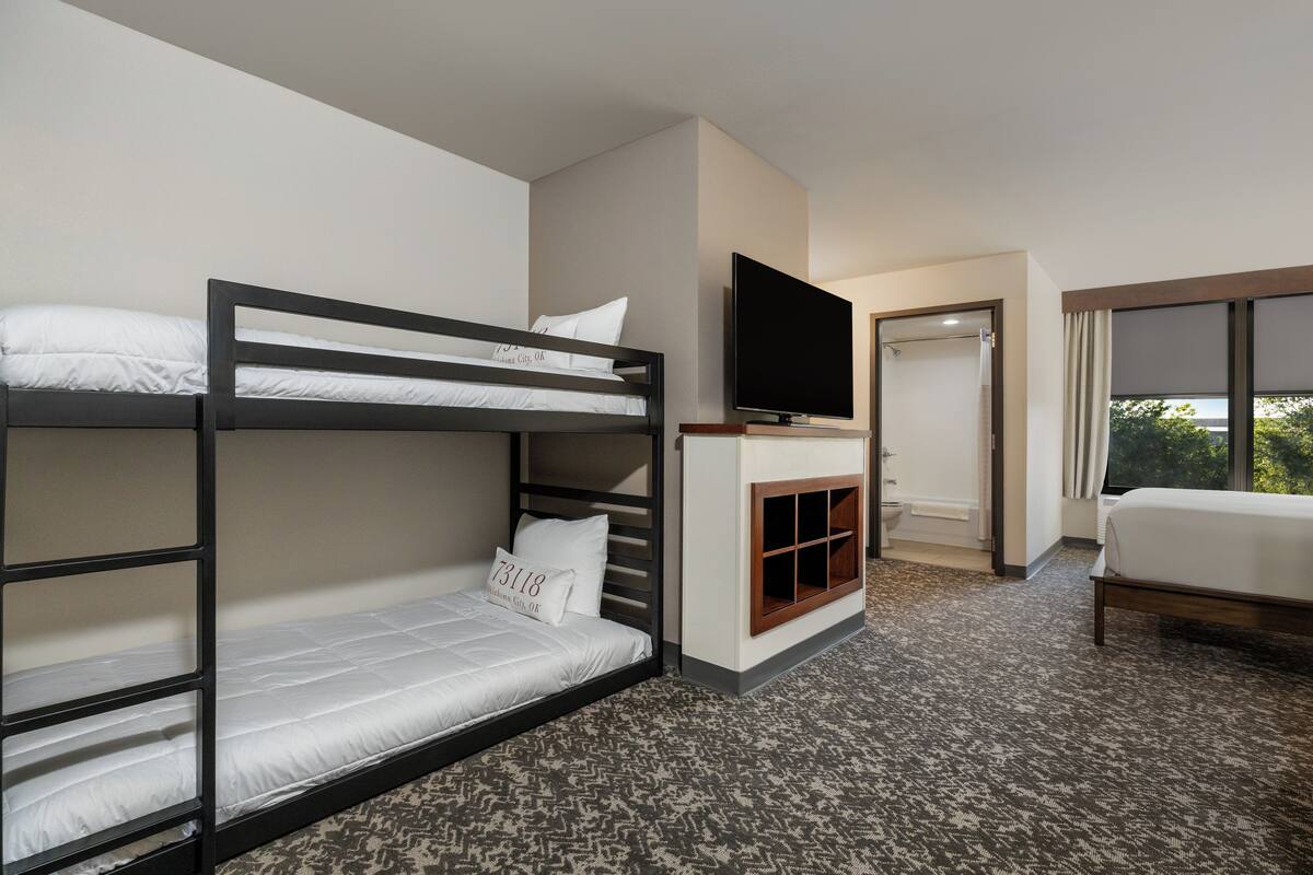 Habitación de hotel con literas, un televisor de pantalla plana, un pequeño rincón de descanso y un ventanal grande.