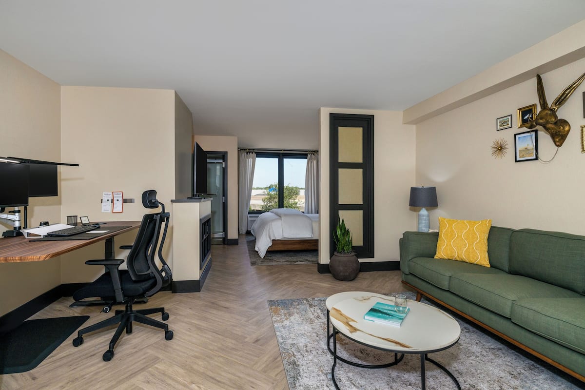 Una habitación de hotel moderna con escritorio, silla de oficina, sofá verde y una cama con vistas.