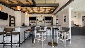 Une cuisine moderne dotée d’un coin bar, avec un îlot central agrémenté de tabourets, d’un éclairage suspendu et d’un plafond orné de poutres apparentes.
