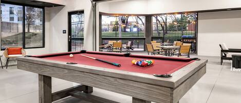 A pool table with balls, chairs, and a glass-enclosed area with a view of the outside.