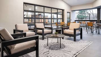 A modern lounge area with sofas and tables, large windows, and a view of the outside.