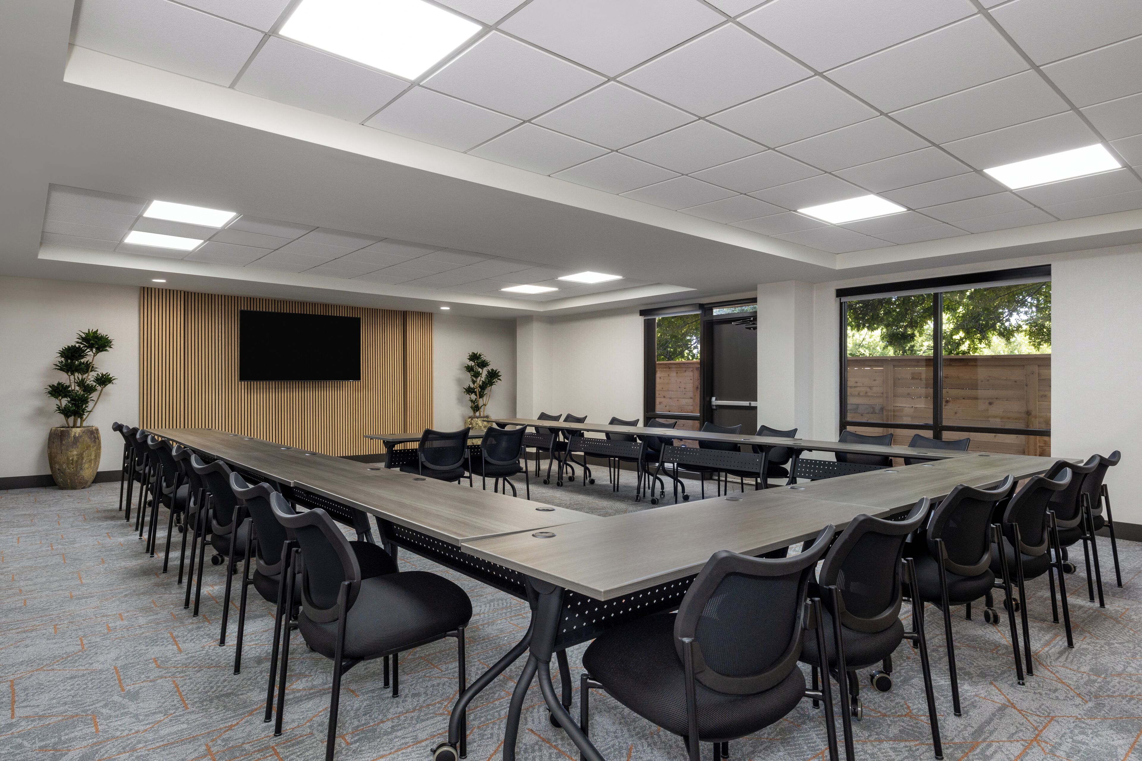 A conference room with a long table, black chairs, a flat-screen TV, and a large window.