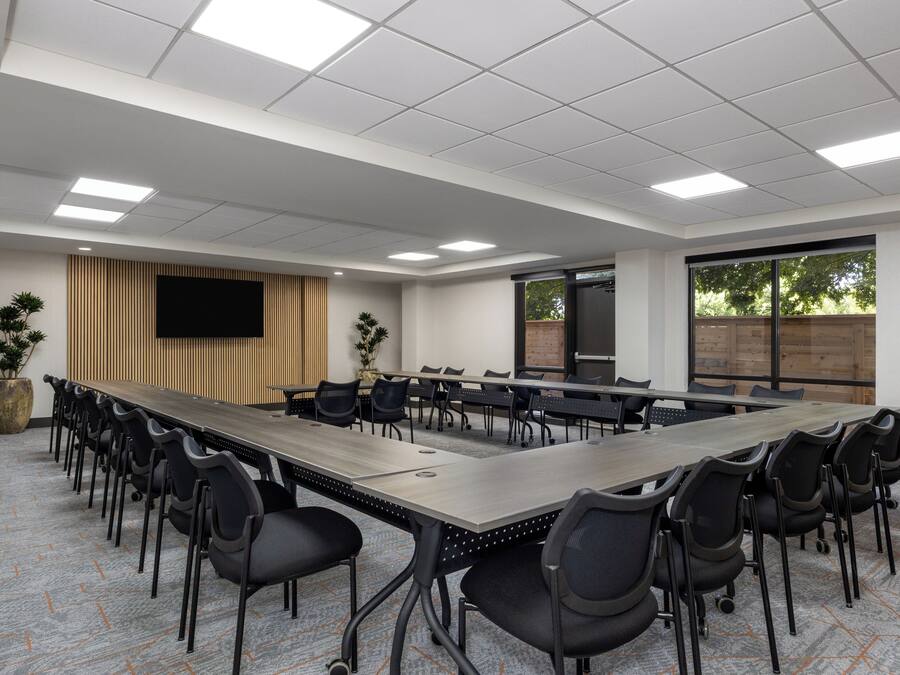 Un salón de conferencias con una larga mesa, sillas negras, un televisor de pantalla plana y un amplio ventanal.