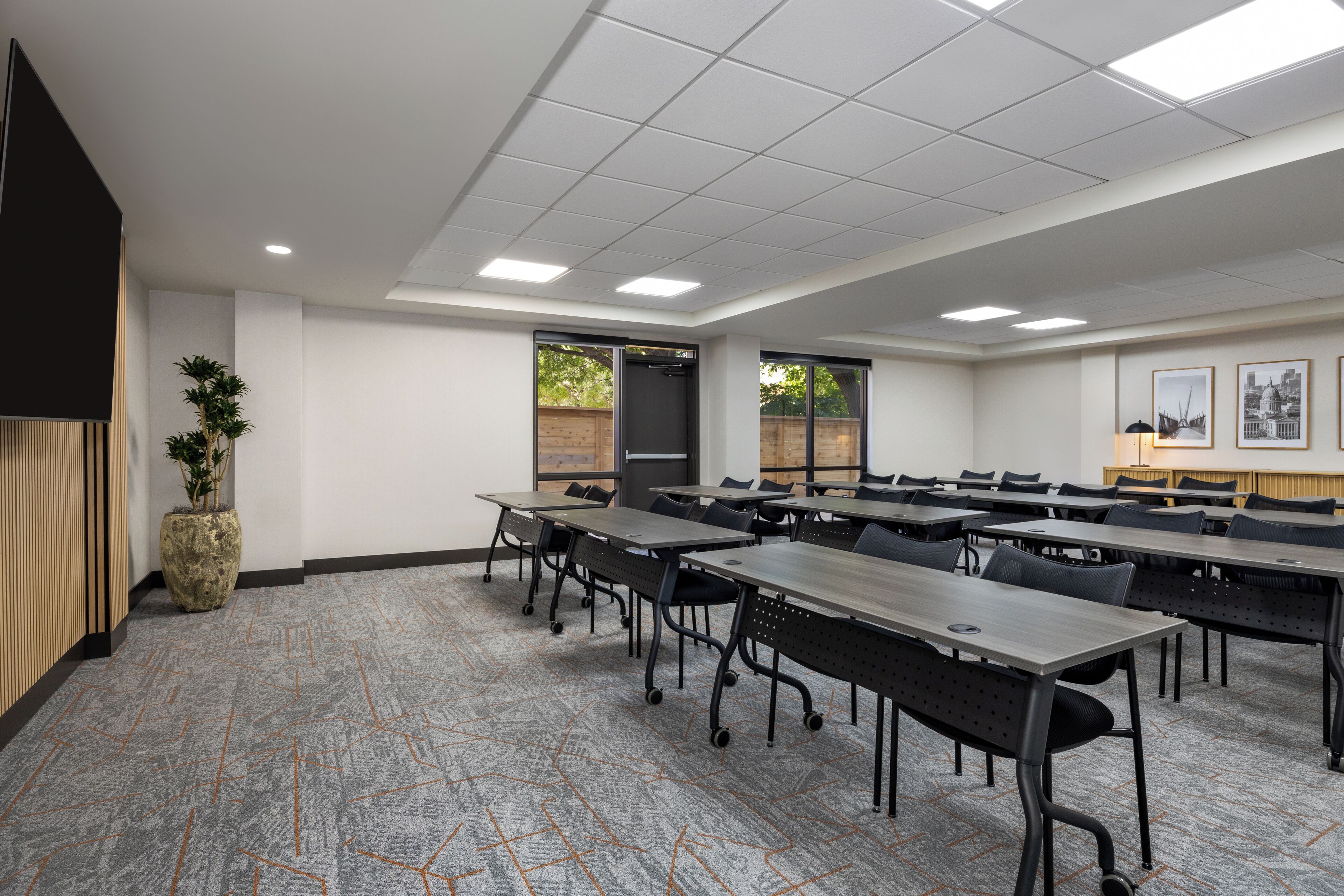 Un salón de conferencias con varias mesas y sillas, una planta grande en maceta, y una puerta que da al exterior.
