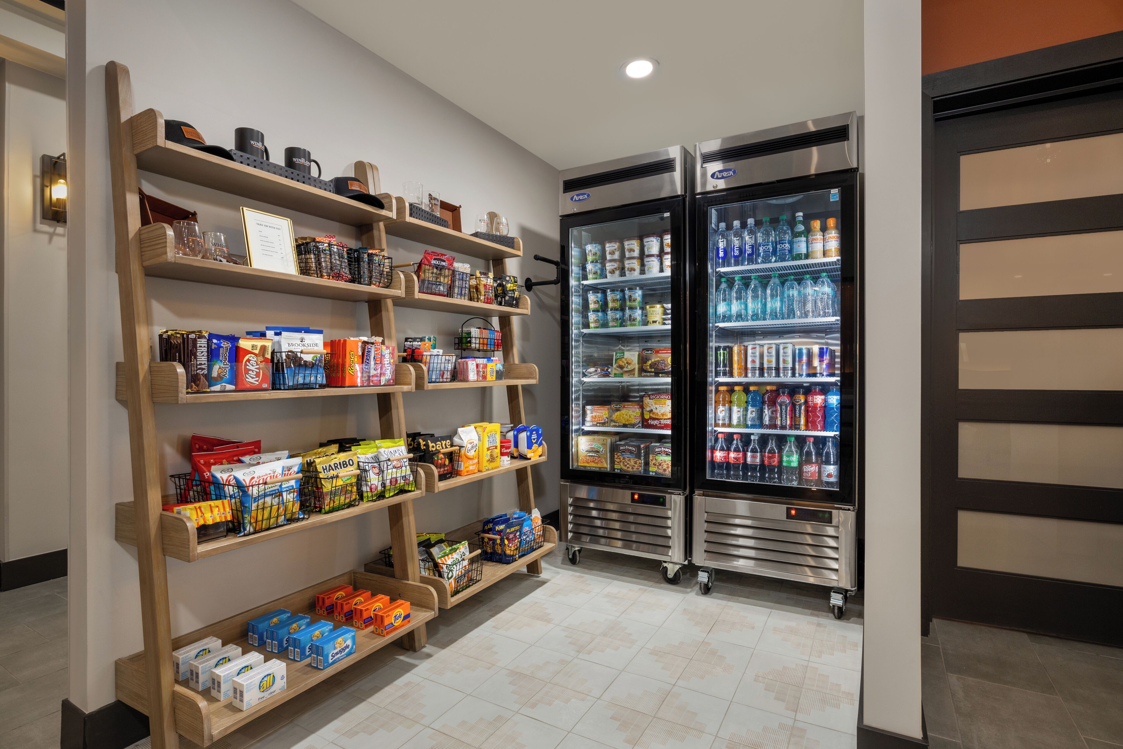 Un espace bien aménagé où l’on peut trouver des collations et des boissons, avec des étagères remplies de produits et deux réfrigérateurs pour les boissons.