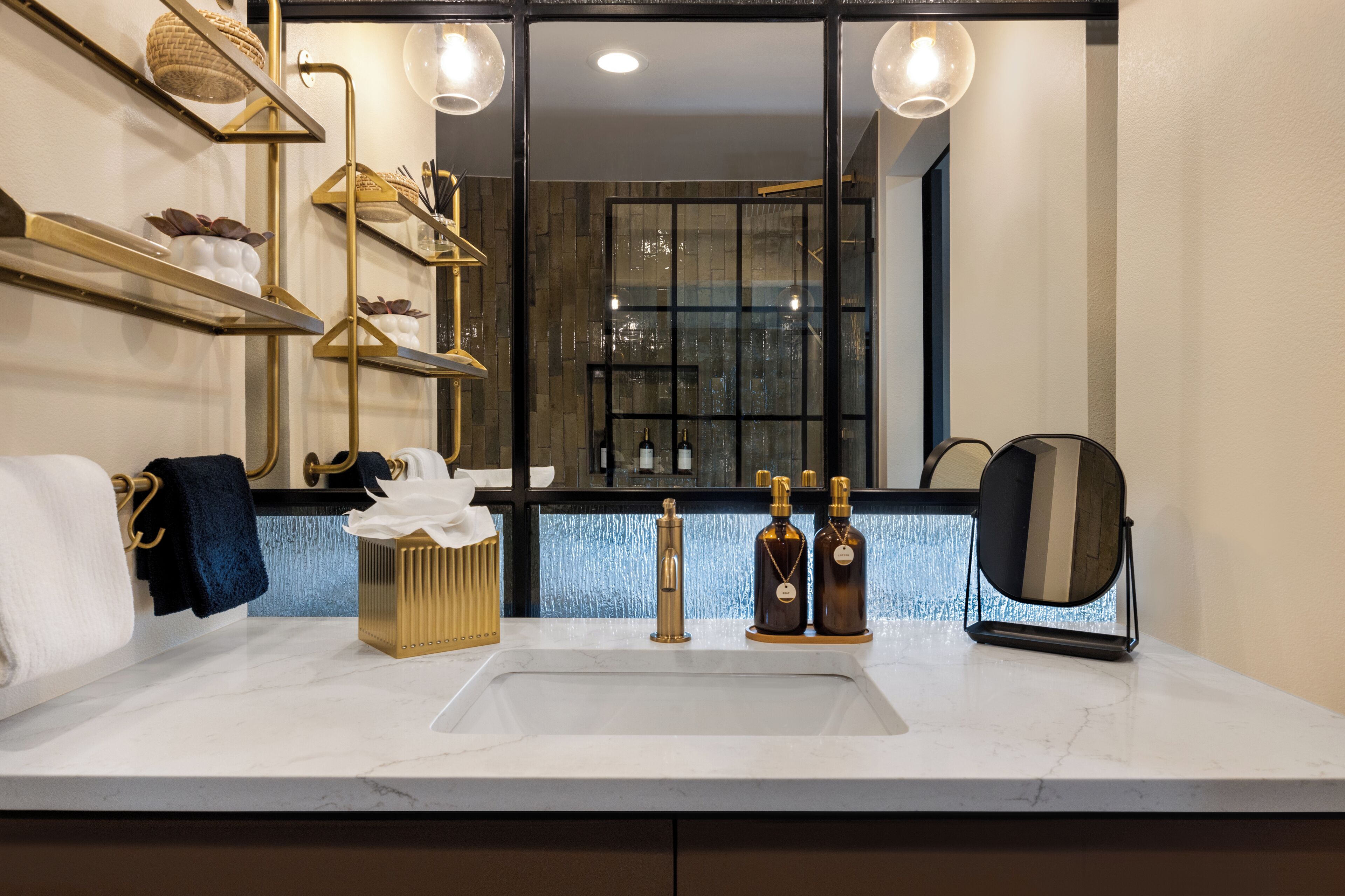 A modern bathroom with a large mirror, a marble sink, and gold fixtures.