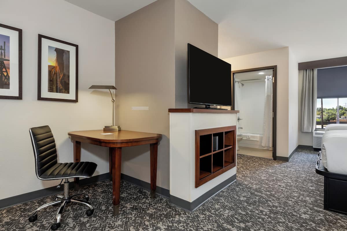 Habitación de hotel con televisor de pantalla plana, escritorio con silla, cama y baño visible a través de una puerta abierta.