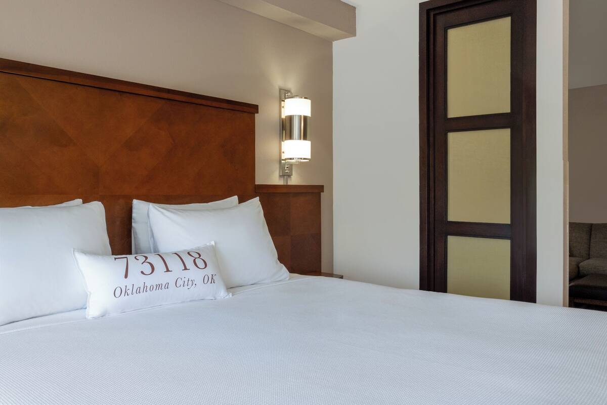 Habitación de hotel con una cama grande, un cabecero de madera, una lámpara fijada a la pared y una puerta con paneles de vidrio.