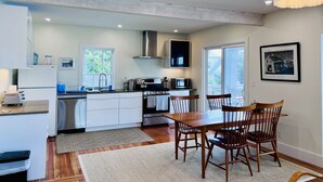 Une cuisine moderne avec des meubles blancs, une cuisinière, un four à micro-ondes et un coin repas comprenant des chaises et une table en bois.