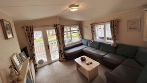 A cozy living room with a sectional sofa, a small wooden coffee table, and a sliding glass door leading to a balcony. - Beautiful 3-bed Selfcontained Lodge Great Yarmouth (Great Yarmouth)