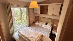 A bedroom with a bed, a bedside table, a lamp, and a window with curtains. - Beautiful 3-bed Selfcontained Lodge Great Yarmouth (Great Yarmouth)