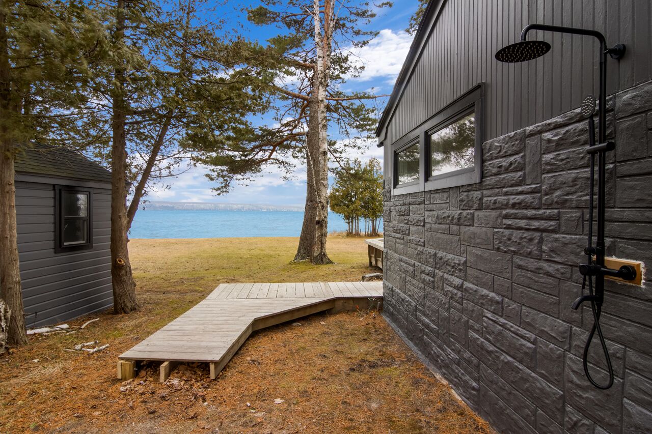 Une cabane avec une façade en pierre, une terrasse en bois donnant sur une plage et une douche attenante.