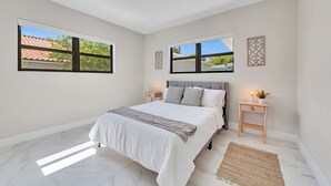 Une chambre avec un grand lit, deux tables de chevet avec des lampes, une fenêtre et un luminaire au plafond.