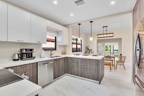 A modern kitchen with white cabinets, a built-in oven, and a dining area with wooden chairs. - Renovated Miami Home, Grill & Gym, Great location, 8 min Brickell, 10 mins Beach (Miami)
