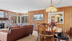 A cozy living room with a stone fireplace, wooden walls, a brown leather sofa, a dining table with chairs, and a chandelier. - Mammoth Getaway, Short walk to the Village and steps to Canyon Lodge shuttle. (Mammoth Lakes)