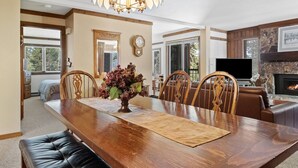 A dining area with a wooden table, leather chairs, and a chandelier. There is a fireplace and a television in the background. - Mammoth Getaway, Short walk to the Village and steps to Canyon Lodge shuttle. (Mammoth Lakes)