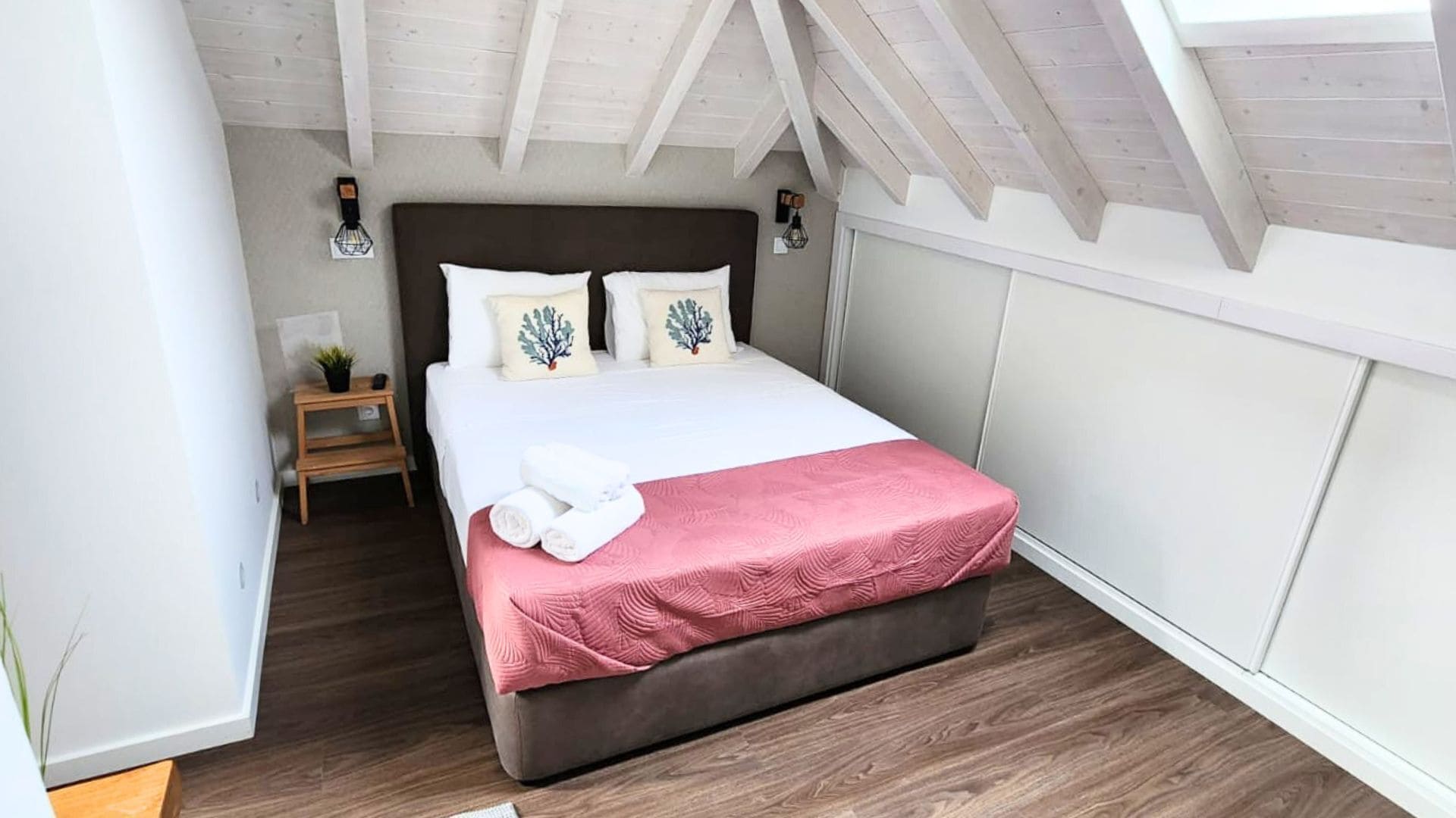 A bedroom with a large bed, wooden floor, white walls, and a sloped ceiling.