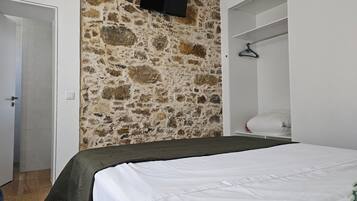 Ein Schlafzimmer mit Stehwand, einem Bett mit weißer Bettwäsche, einem Kleiderschrank und einem an der Wand montierten Fernseher.