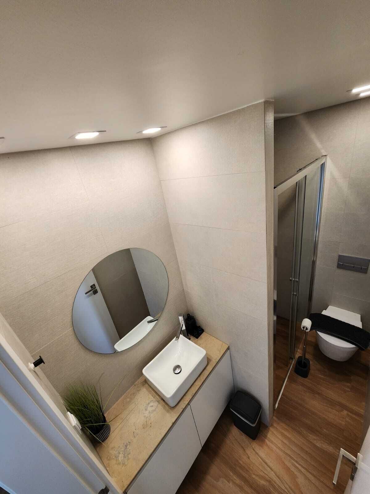 Un baño moderno con un espejo redondo, un lavabo, un inodoro y una zona de ducha.