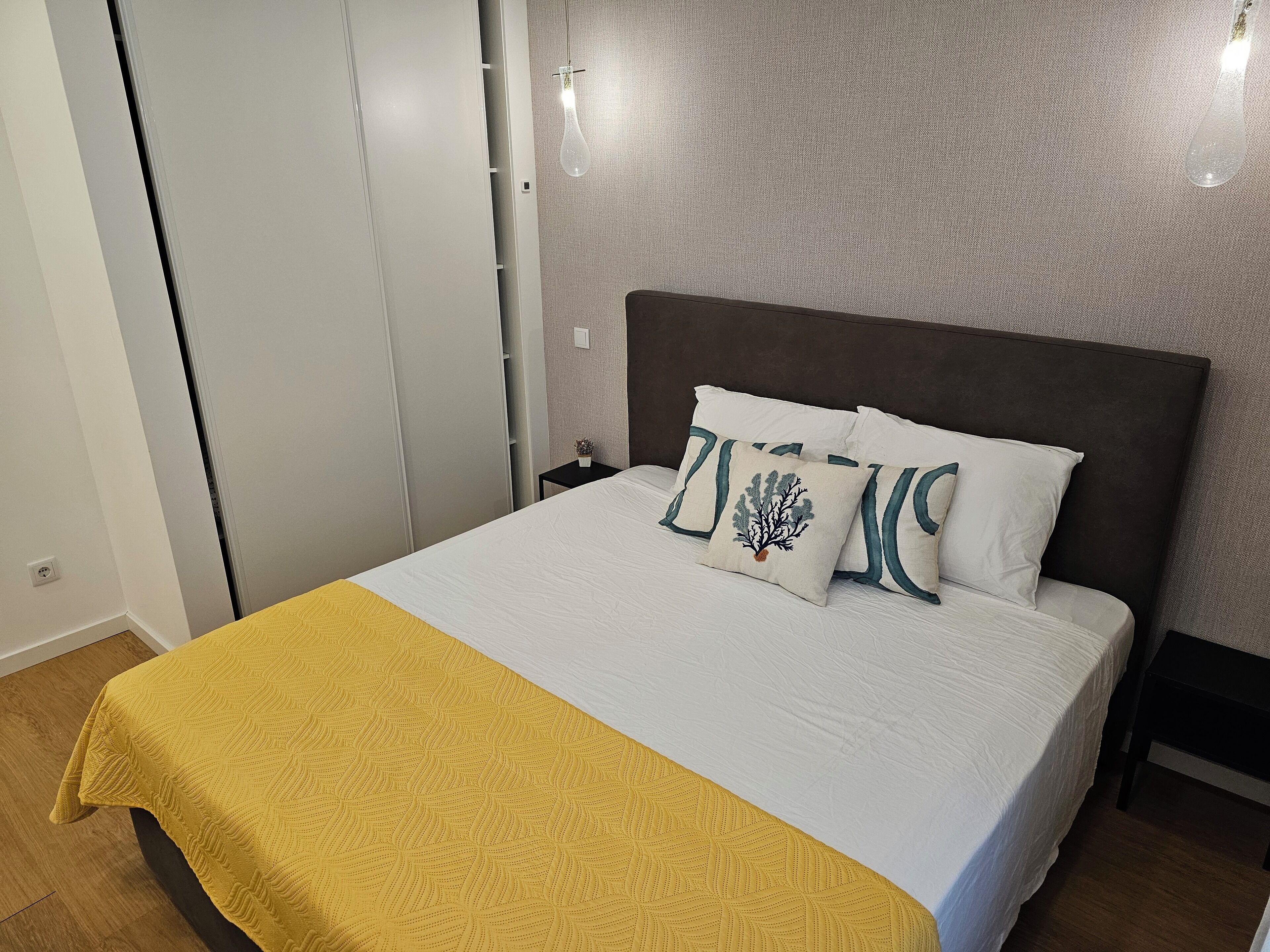 A neatly made bed with a yellow blanket, white pillows, and a dark headboard.