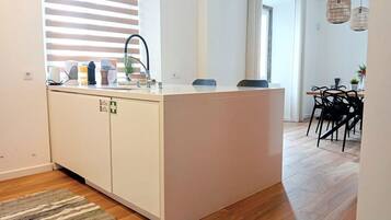 Een moderne keuken met een wit kookeiland, een spoelbak en een eethoek met zwarte stoelen.