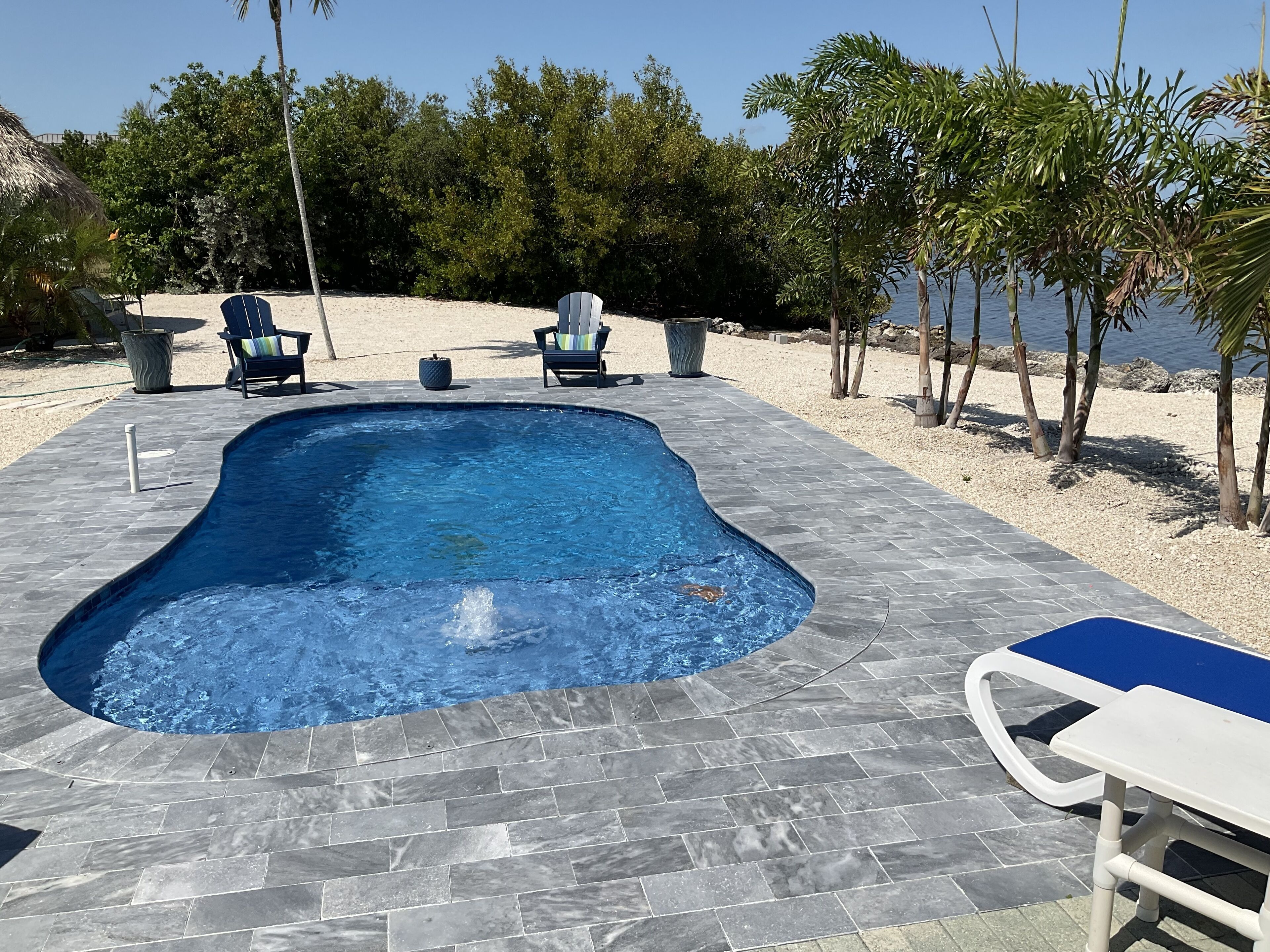 Une piscine entourée d’une terrasse en pierre, avec des chaises et une table.