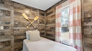 Un dormitorio con paredes de paneles de madera, una cama con ropa blanca y una ventana con cortinas rosa y blanca.