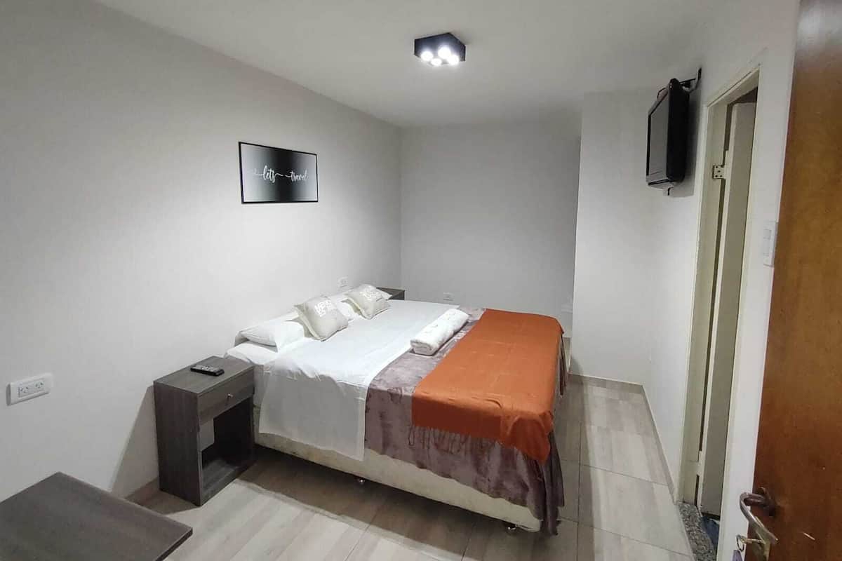 A small, neatly arranged bedroom with a bed, bedside table, and a TV mounted on the wall.