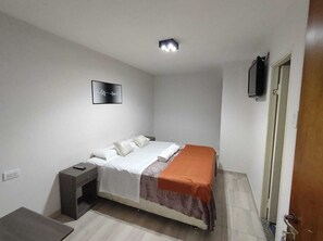 Una camera da letto piccola e ordinata, con un letto, un comodino e una TV montata a parete.