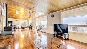 Un salón amplio con techo de madera, una mesa de centro de vidrio, chimenea y un ventanal grande.