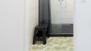 A small, enclosed shower area with a showerhead, a curtain, and a black stool. - Robin Wood Apartment (Vienna)