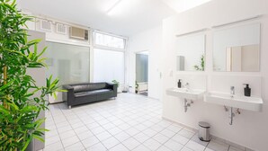 A modern bathroom with white tiles, two sinks, a mirror, and a black leather sofa in a spacious room. - Robin Wood Apartment (Vienna)