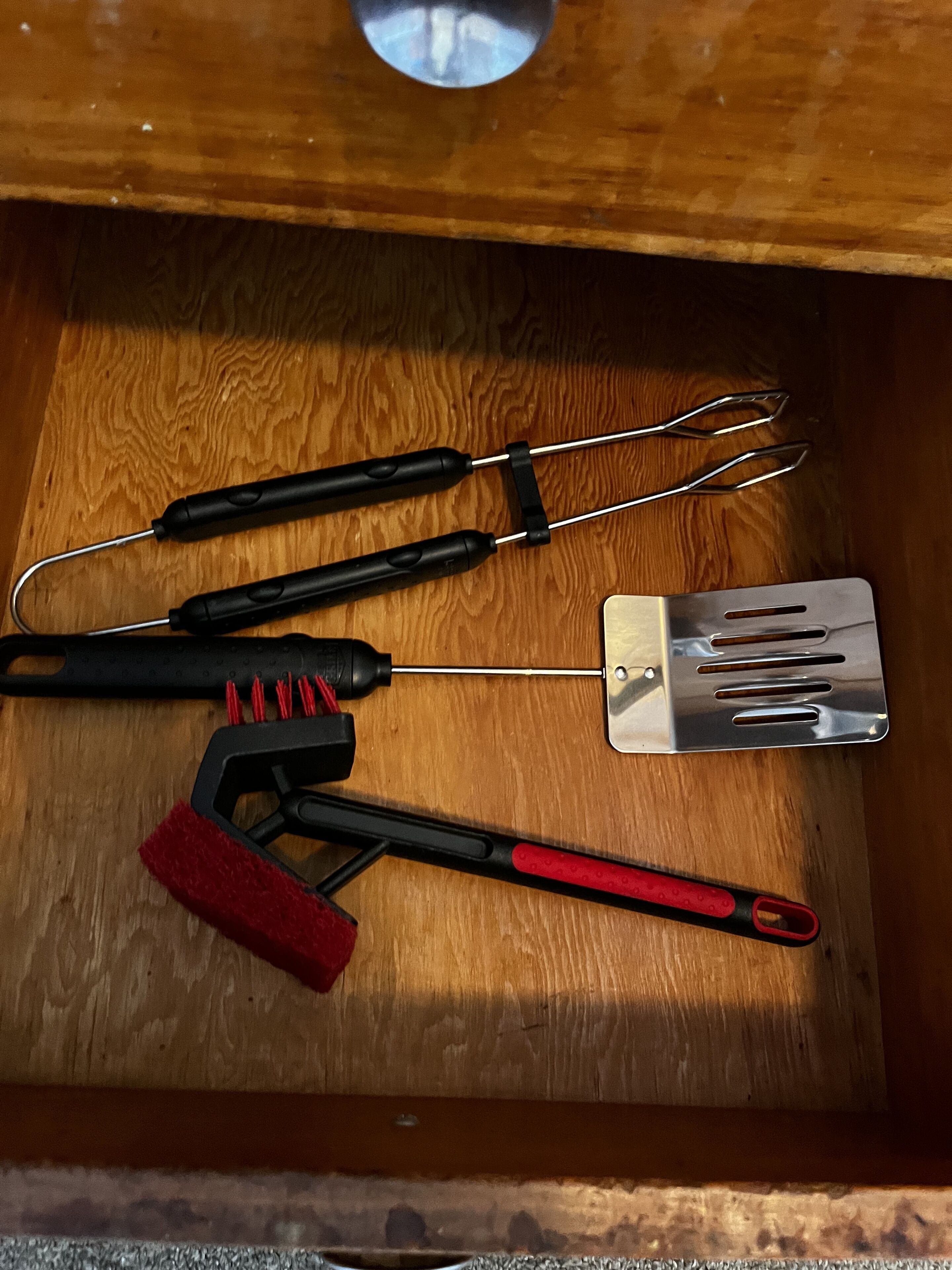 Un cassetto che contiene una spatola metallica, una spazzola nera e rossa, un attrezzo nero con un gancio e un attrezzo nero con un manico lungo.