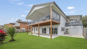 Une maison moderne à deux étages, dotée d’un balcon, d’une terrasse couverte et d’une pelouse bien entretenue.