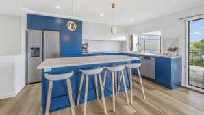 Une cuisine moderne avec des meubles de couleur bleue, un plan de travail blanc et quatre tabourets de bar.