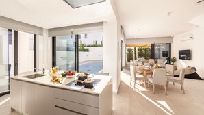 A modern kitchen with a large island, a dining area with a table and chairs, and a view of a swimming pool. - Protaras Periyiali Seaside Villa 33 (Protaras)
