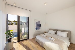 A modern bedroom with a large bed, a potted plant, a painting, and a view through a sliding door.