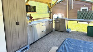 A covered outdoor kitchen with a sink, countertop, and cabinets.