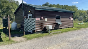 A rustic, single-story building with a metal roof and wooden siding, featuring a 'MEN' and 'WOMEN' sign on the side.
