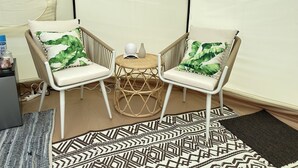 A room with two white wicker chairs with green leaf-patterned cushions, a small round table with a white vase, and a patterned rug.