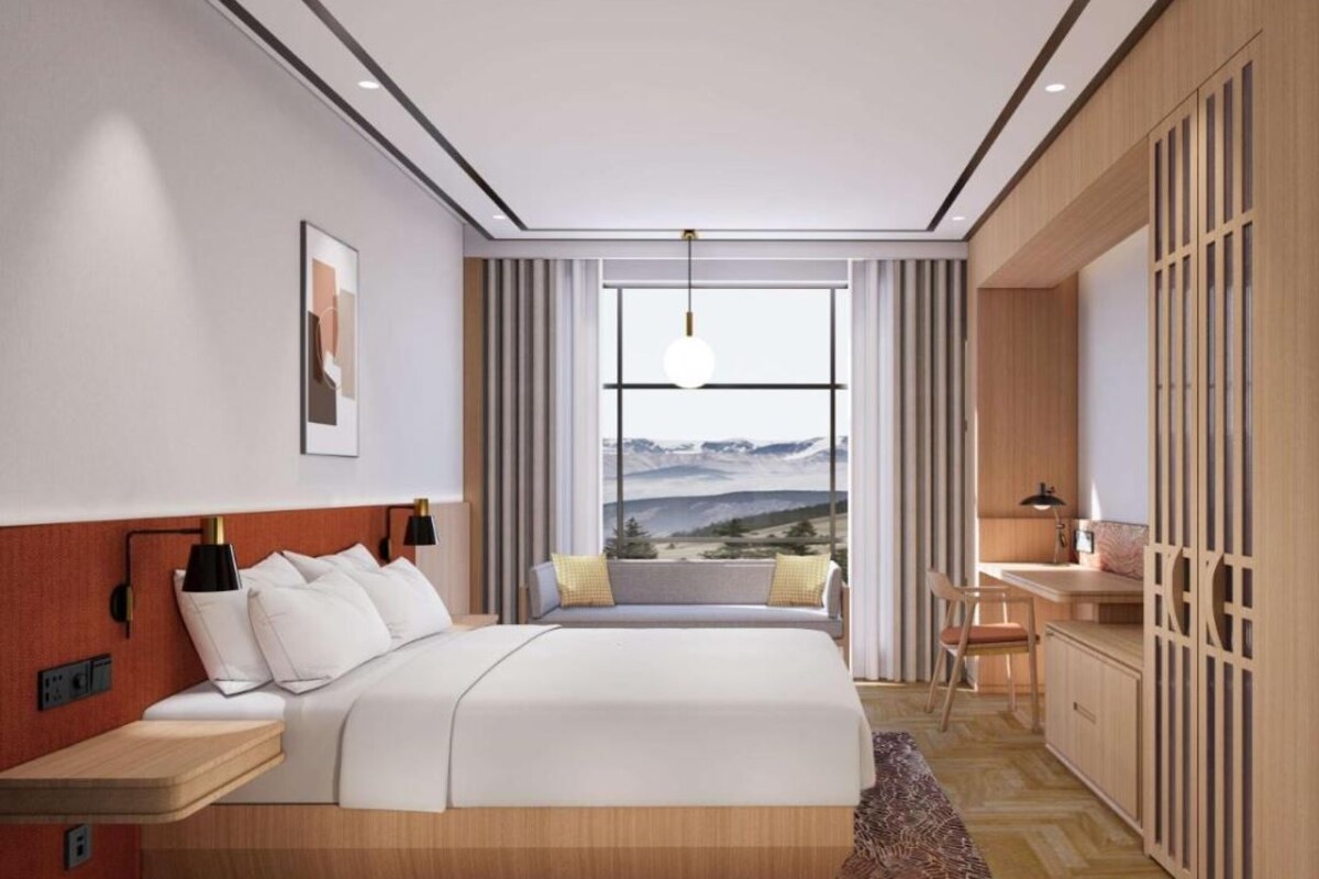 A modern hotel room with a large bed, a desk, and a view of the mountains.