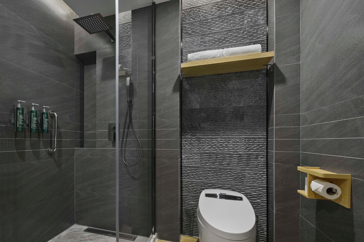A modern bathroom with a glass-enclosed shower, a toilet, and a shelf with toiletries.