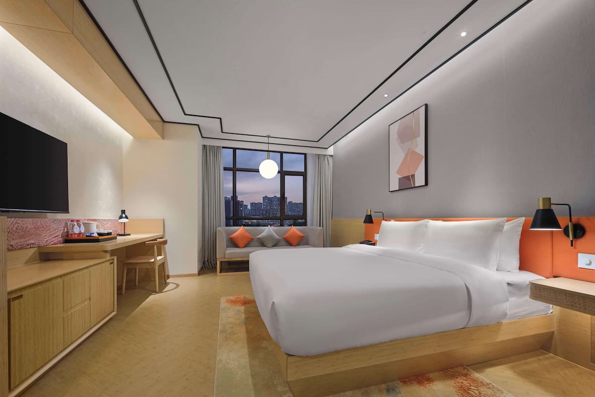 Ein modernes Hotelzimmer mit einem großen Bett, einem Schreibtisch, einem Fernseher und Blick auf die Stadt.