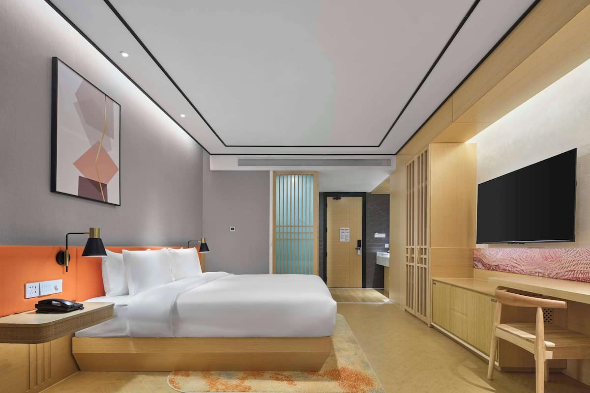 Ein modernes Hotelzimmer mit einem Bett, Nachttisch, Lampe und einem Fernseher auf einem Holzkasten.