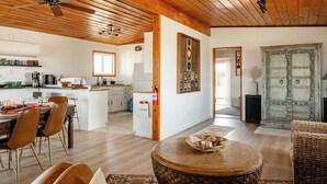 Un'ampia zona giorno con soffitto in legno, un tavolo da pranzo apparecchiato e un angolo salotto accogliente con un tavolino rotondo.