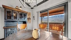Ein Essbereich mit Holztisch, Stühlen, einer Zierblume und Blick durch große Fenster.
