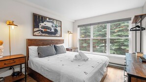 A neatly arranged bedroom with a large bed, bedside tables, a desk, and a window with a forest view. -  Etta Place 6 by AvantStay | Ski In/ Ski Out Unit! (Telluride)