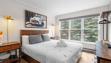 A neatly arranged bedroom with a large bed, bedside tables, a desk, and a window with a forest view.