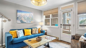 A living room with a blue sofa, a wooden coffee table, a map on the wall, and a door leading outside.