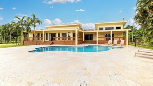 Una moderna casa a due piani con piscina, circondata da palme e un prato curato.
